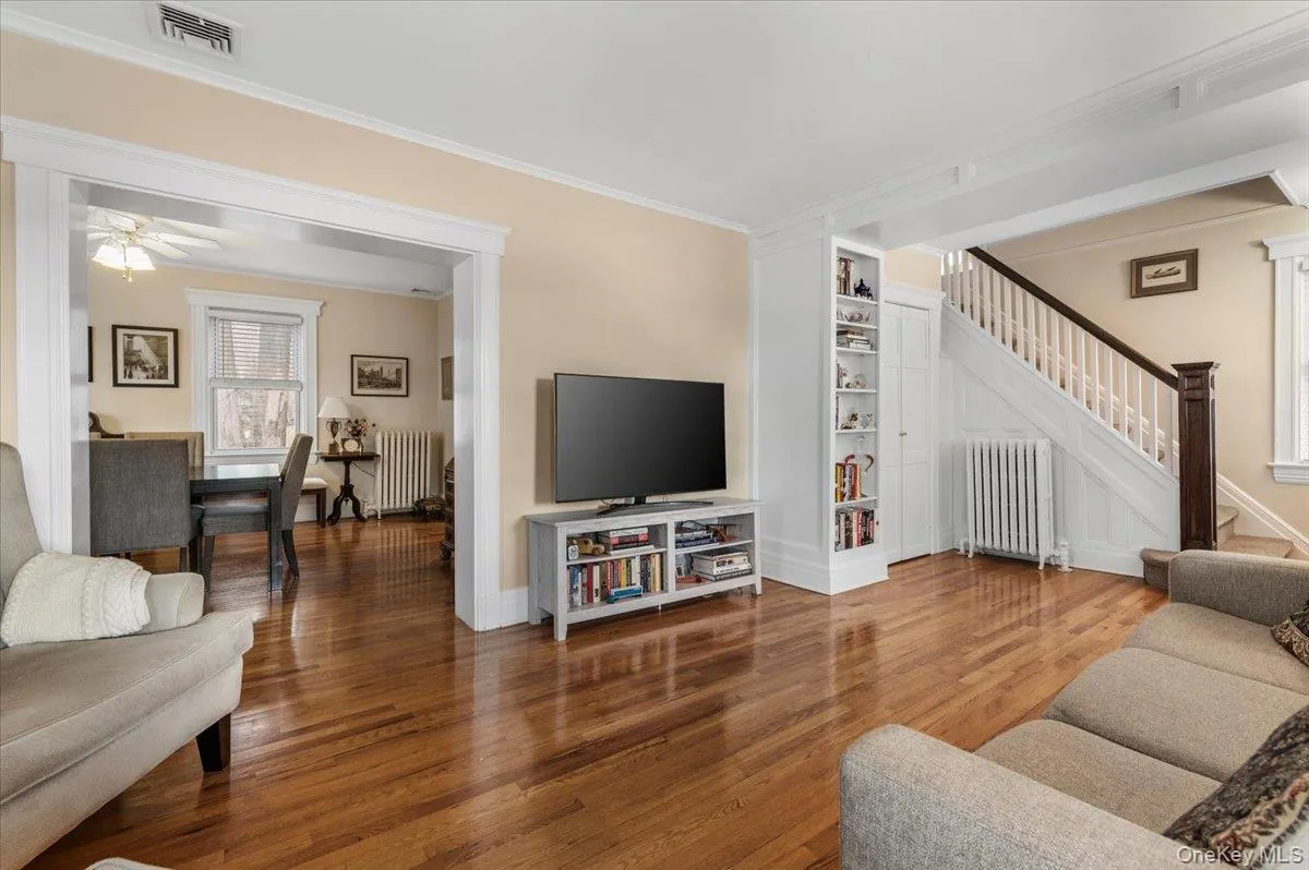 Living room with stairway, radiator, wood finished floors, ornamental molding, and built in shelves Living room with stairway, radiator, wood finished floors, ornamental molding, and built in shelves