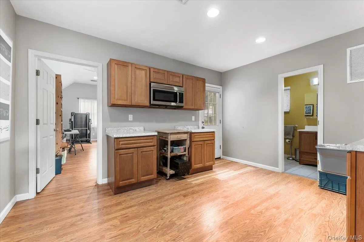 Kitchen with light wood-style floors, stainless steel microwave, brown cabinets, and recessed lighting Kitchen with light wood-style floors, stainless steel microwave, brown cabinets, and recessed lighting