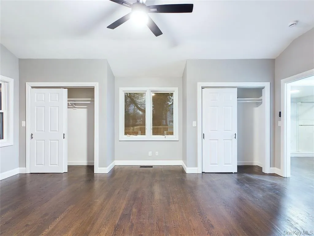 Unfurnished bedroom with two closets, dark wood-style flooring, and ceiling fan Unfurnished bedroom with two closets, dark wood-style flooring, and ceiling fan