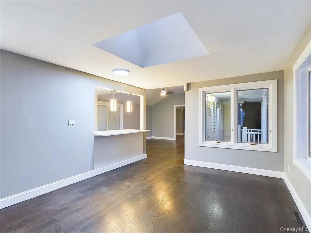 Unfurnished room featuring dark wood-style floors, lofted ceiling, and a skylight Unfurnished room featuring dark wood-style floors, lofted ceiling, and a skylight