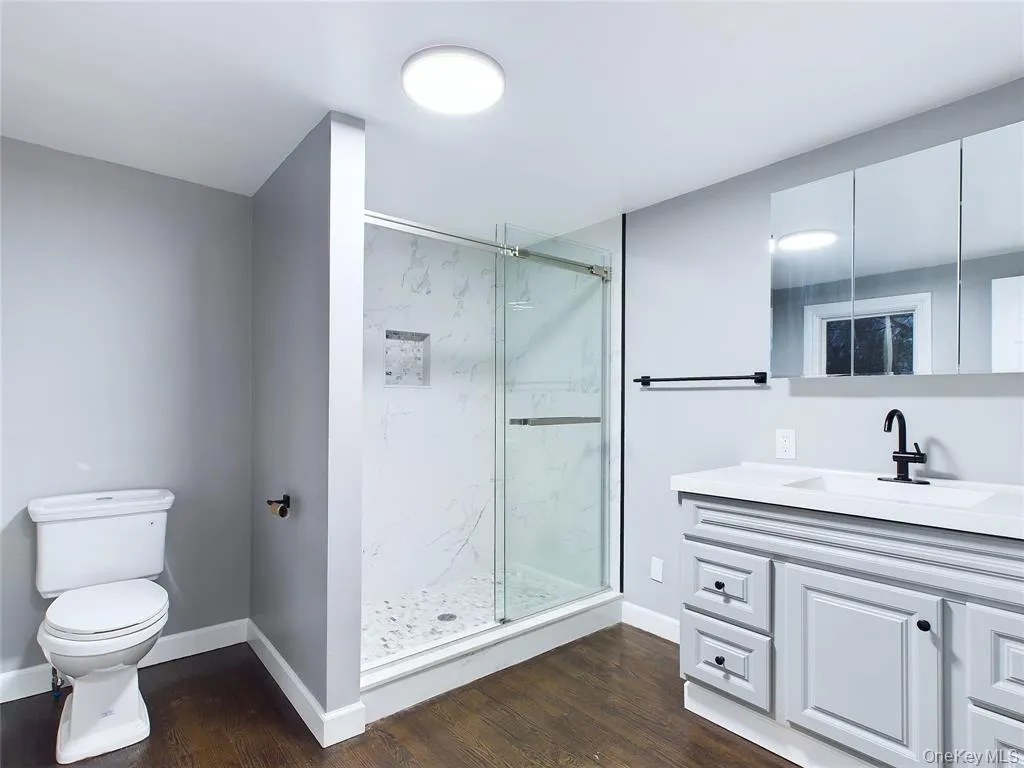 Full bath with vanity, dark wood-style flooring, and a marble finish shower Full bath with vanity, dark wood-style flooring, and a marble finish shower