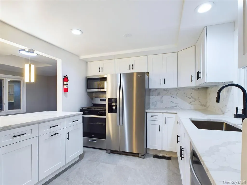Kitchen with white cabinetry, light stone counters, appliances with stainless steel finishes, backsplash, and recessed lighting Kitchen with white cabinetry, light stone counters, appliances with stainless steel finishes, backsplash, and recessed lighting