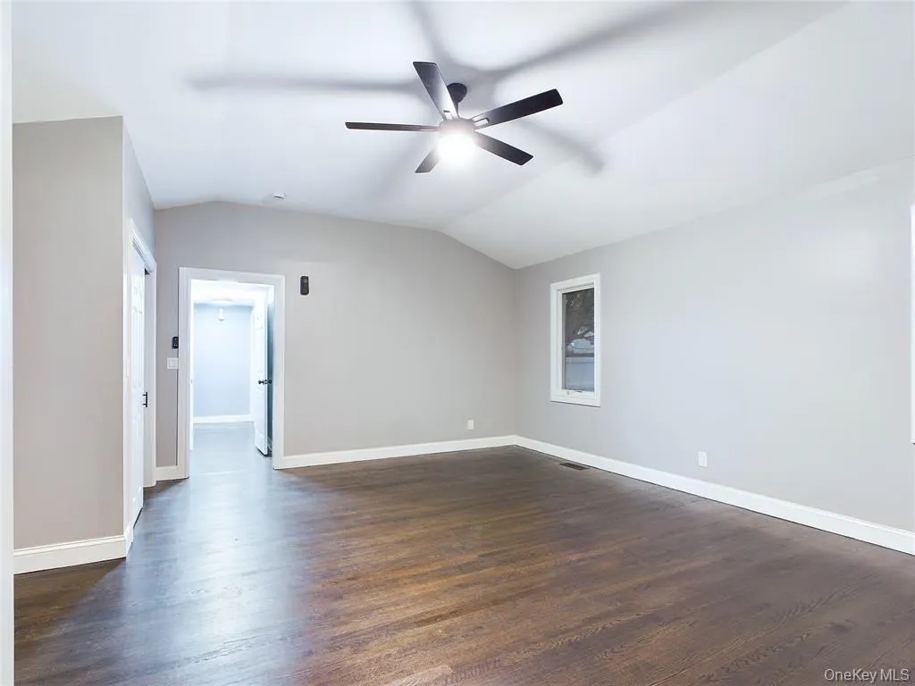 Empty room featuring dark wood finished floors, lofted ceiling, and a ceiling fan Empty room featuring dark wood finished floors, lofted ceiling, and a ceiling fan