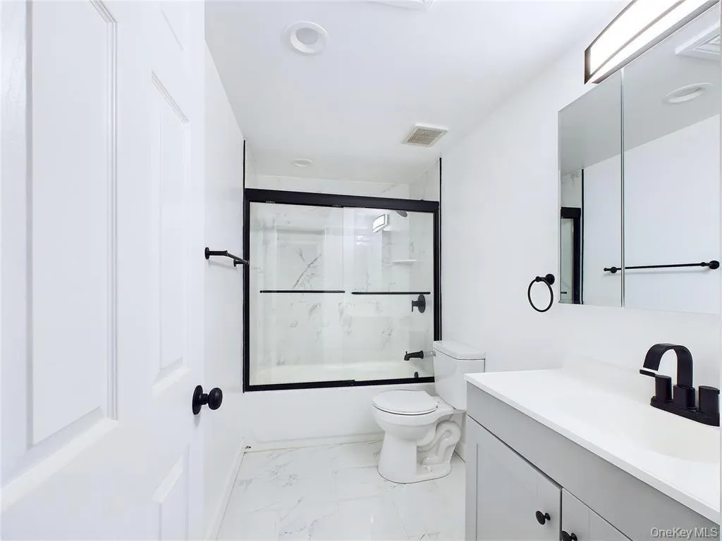 Full bathroom featuring light marble finish flooring, bath / shower combo with glass door, and vanity Full bathroom featuring light marble finish flooring, bath / shower combo with glass door, and vanity