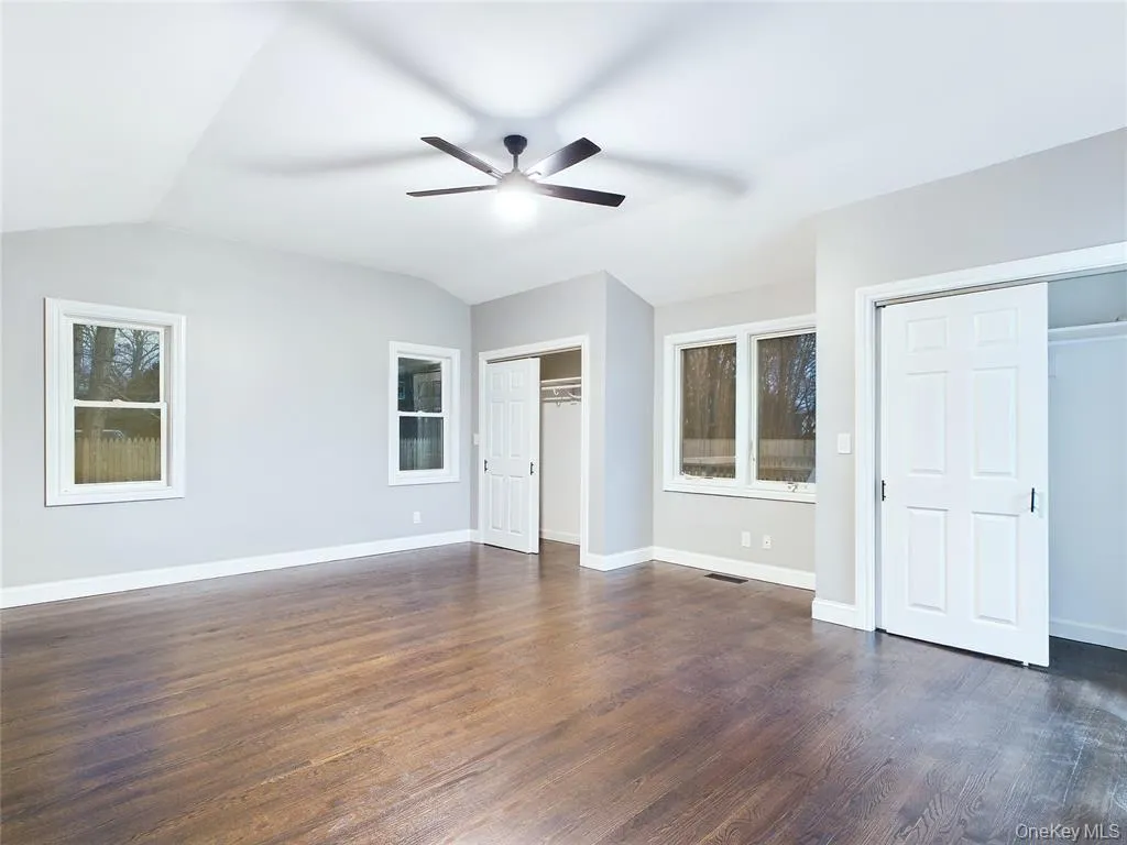 Unfurnished bedroom featuring two closets, dark wood-style floors, vaulted ceiling, and a ceiling fan Unfurnished bedroom featuring two closets, dark wood-style floors, vaulted ceiling, and a ceiling fan