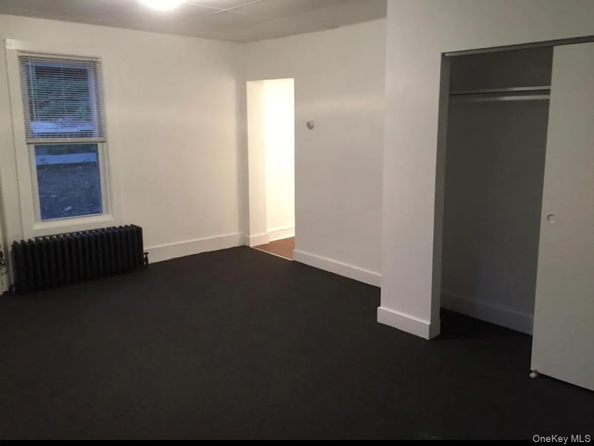 Unfurnished bedroom featuring radiator heating unit and dark colored carpet Unfurnished bedroom featuring radiator heating unit and dark colored carpet