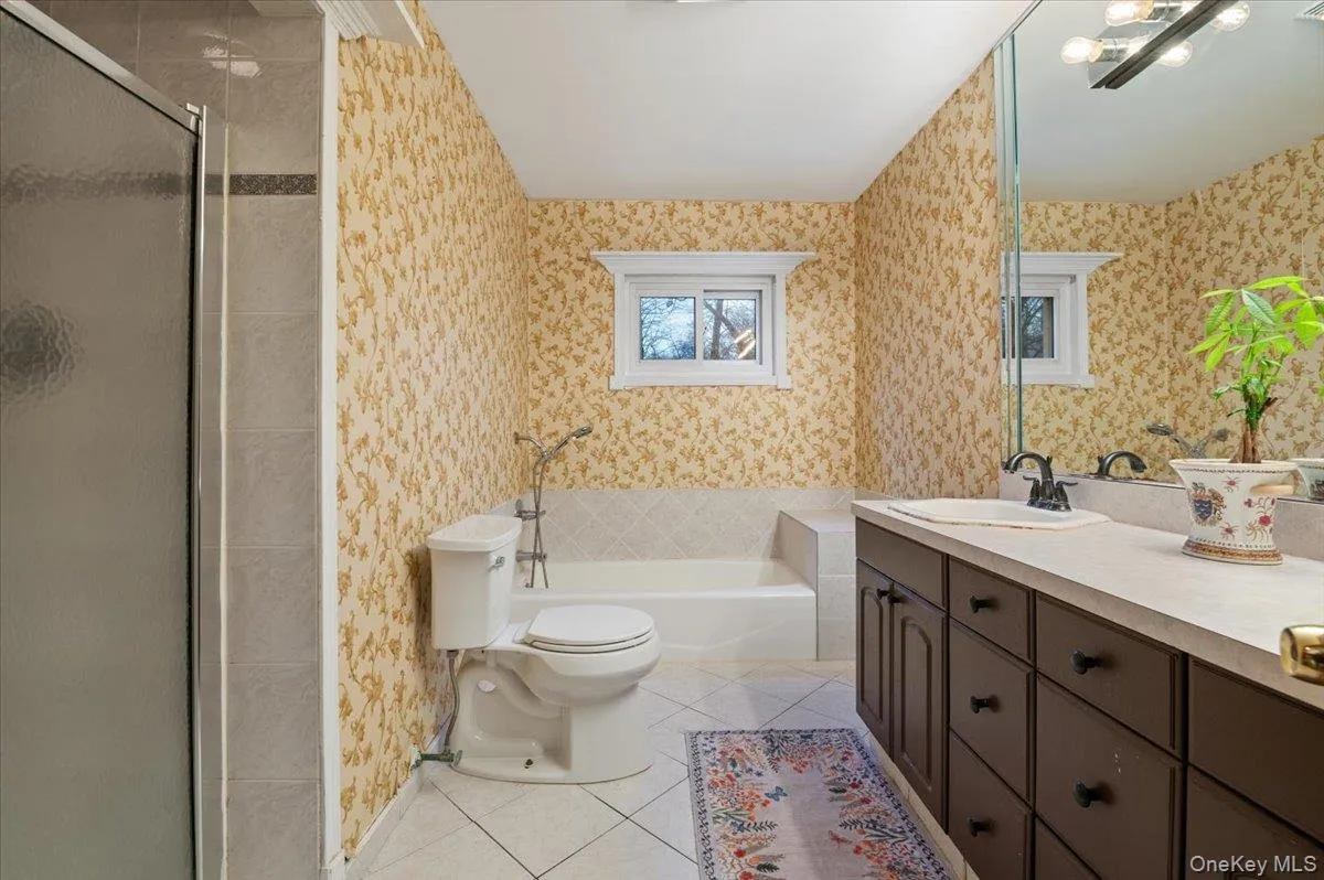 Bathroom featuring wallpapered walls, light tile patterned flooring, a stall shower, vanity, and a garden tub Bathroom featuring wallpapered walls, light tile patterned flooring, a stall shower, vanity, and a garden tub