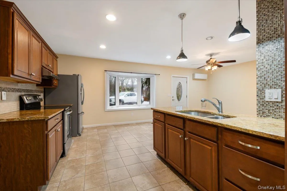 Kitchen with decorative backsplash, brown cabinetry, stainless steel electric range, pendant lighting, and recessed lighting Kitchen with decorative backsplash, brown cabinetry, stainless steel electric range, pendant lighting, and recessed lighting