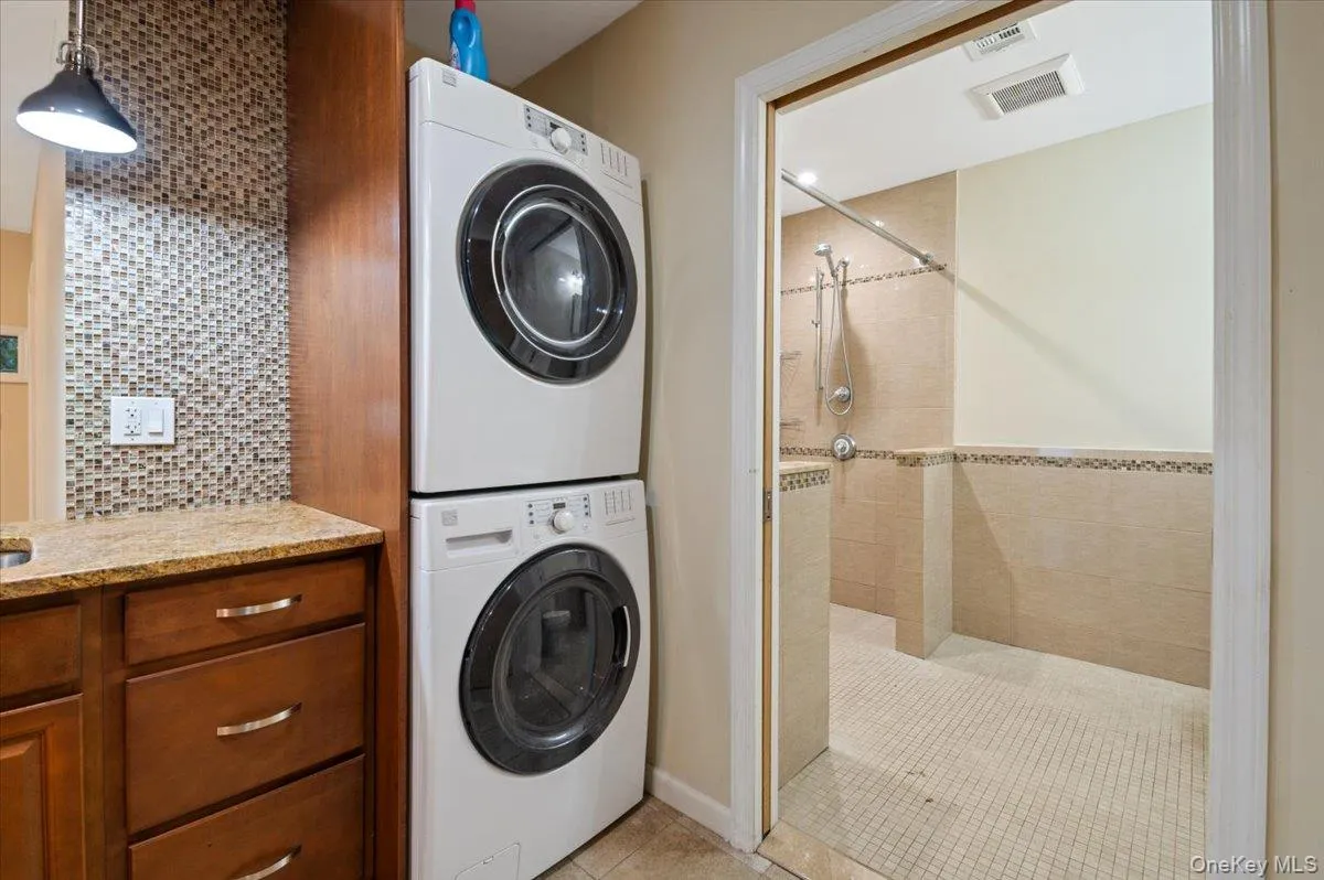 Laundry area featuring stacked washer and clothes dryer and light tile patterned floors Laundry area featuring stacked washer and clothes dryer and light tile patterned floors