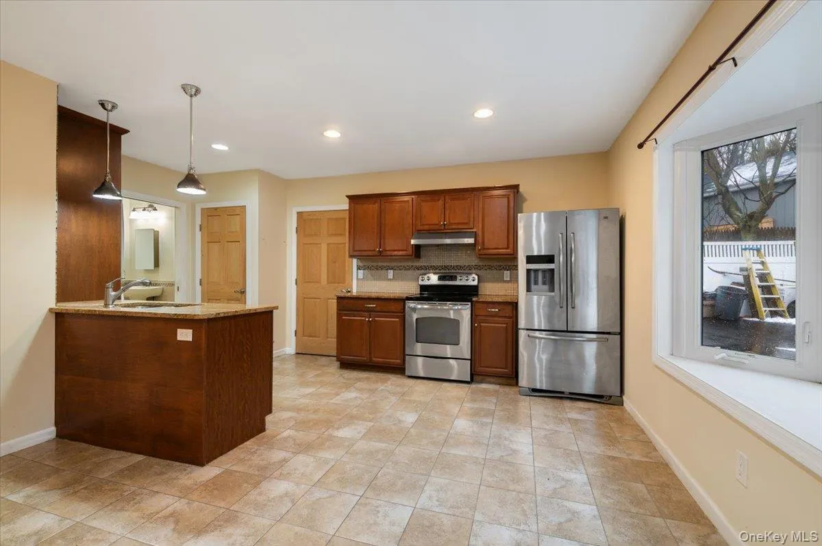 Apartment Kitchen featuring stainless steel appliances, decorative backsplash, hanging light fixtures, brown cabinets, and light stone countertops Apartment Kitchen featuring stainless steel appliances, decorative backsplash, hanging light fixtures, brown cabinets, and light stone countertops