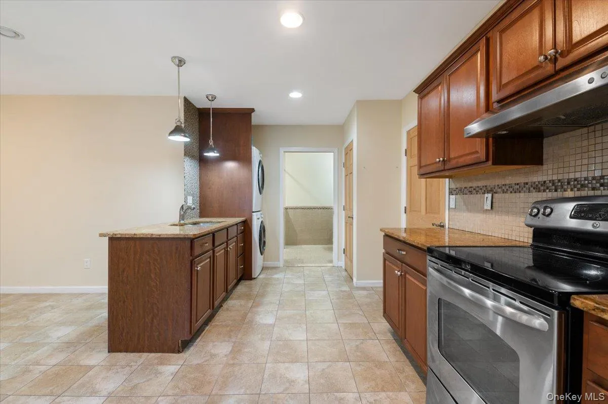 Kitchen featuring stainless steel electric range, light stone counters, estacked washer and dryer, pendant lighting, and recessed lighting Kitchen featuring stainless steel electric range, light stone counters, estacked washer and dryer, pendant lighting, and recessed lighting