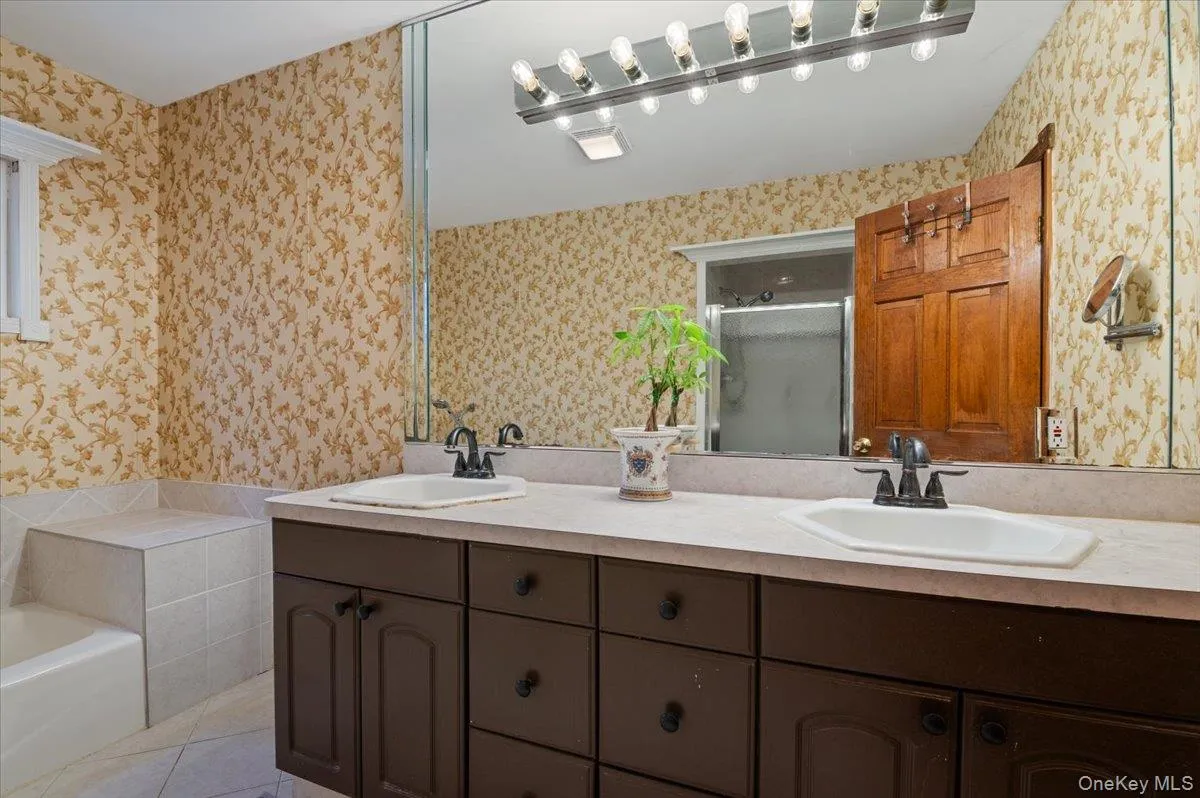 Full bath with double vanity, a shower stall, a bath, wallpapered walls, and light tile patterned floors Full bath with double vanity, a shower stall, a bath, wallpapered walls, and light tile patterned floors