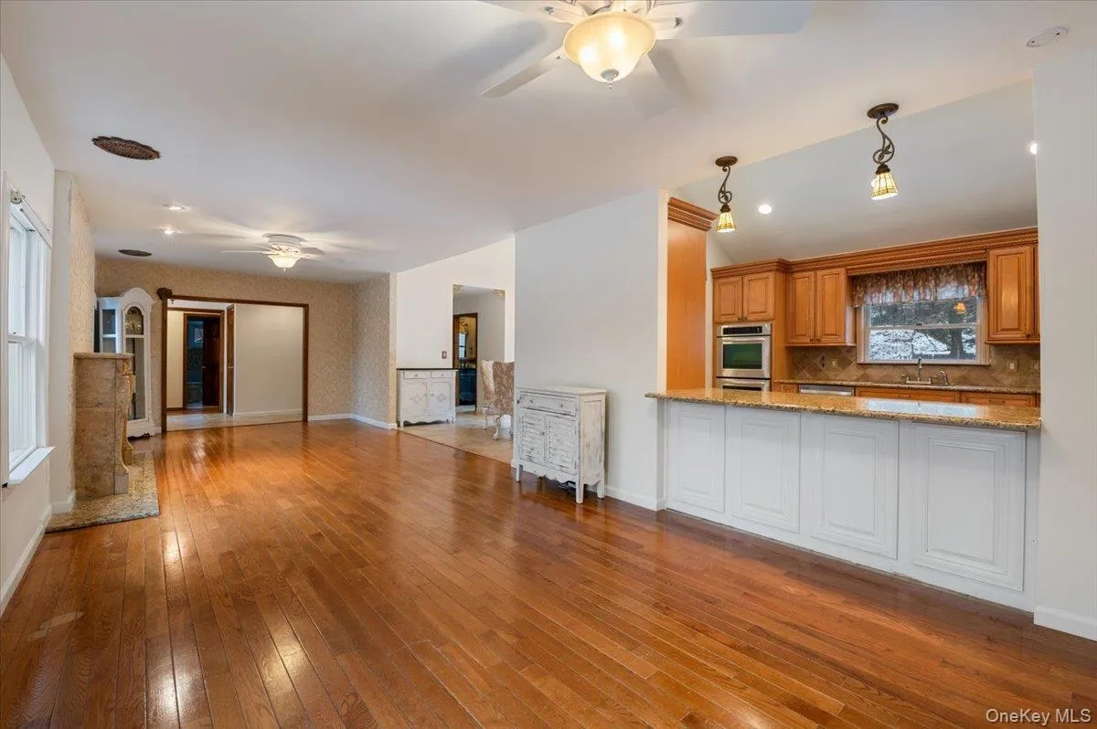 Kitchen featuring a ceiling fan, brown cabinetry, open floor plan, hanging light fixtures, and light stone counters Kitchen featuring a ceiling fan, brown cabinetry, open floor plan, hanging light fixtures, and light stone counters
