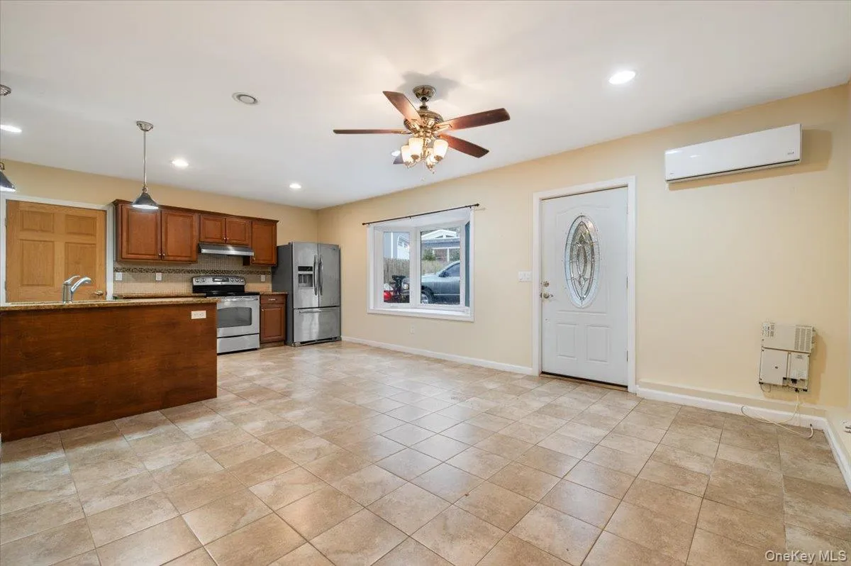 Kitchen featuring brown cabinets, stainless steel appliances, ceiling fan, hanging light fixtures, and a wall mounted AC Kitchen featuring brown cabinets, stainless steel appliances, ceiling fan, hanging light fixtures, and a wall mounted AC