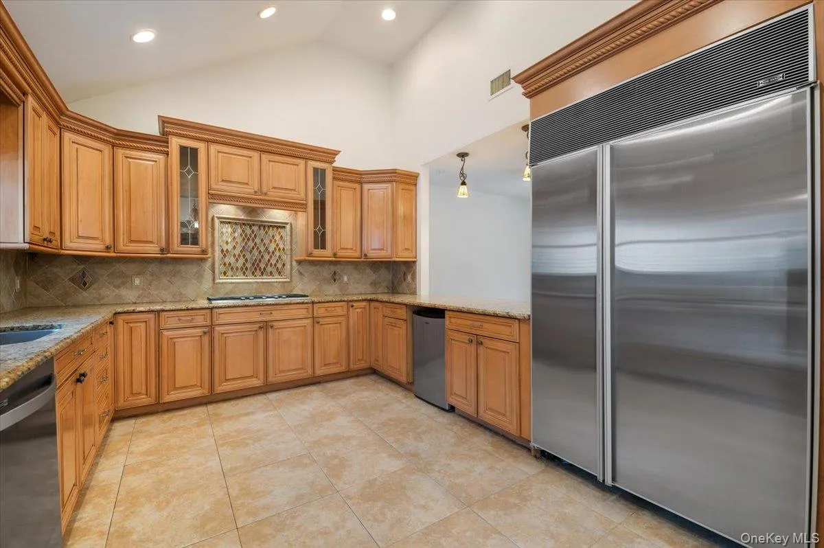 Kitchen featuring stainless steel appliances, hanging light fixtures, light stone countertops, high vaulted ceiling, and tasteful backsplash Kitchen featuring stainless steel appliances, hanging light fixtures, light stone countertops, high vaulted ceiling, and tasteful backsplash