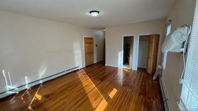 Unfurnished bedroom with baseboard heating and dark wood-style floors Unfurnished bedroom with baseboard heating and dark wood-style floors