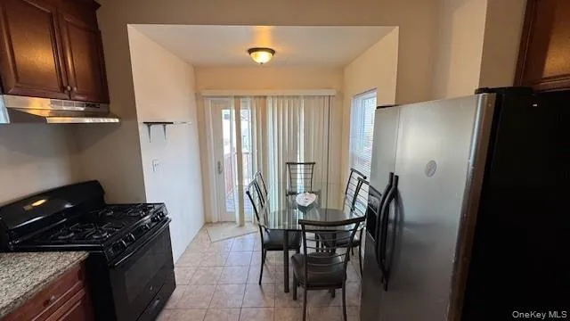 Kitchen with black gas range oven, stainless steel refrigerator with ice dispenser, under cabinet range hood, light tile patterned floors, and light stone countertops Kitchen with black gas range oven, stainless steel refrigerator with ice dispenser, under cabinet range hood, light tile patterned floors, and light stone countertops