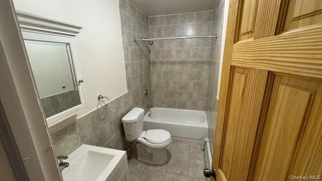 Full bathroom with tile walls, bathtub / shower combination, light tile patterned floors, vanity, and a baseboard heating unit Full bathroom with tile walls, bathtub / shower combination, light tile patterned floors, vanity, and a baseboard heating unit