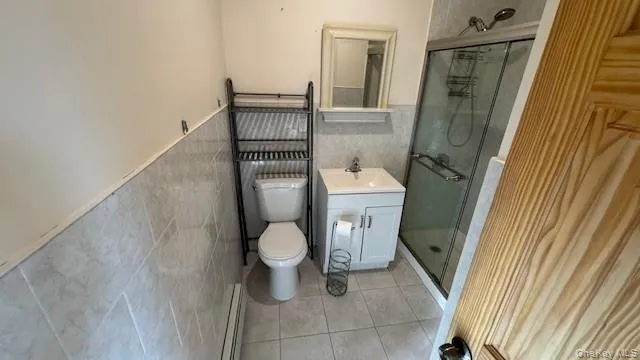 Bathroom with wainscoting, tile walls, vanity, light tile patterned flooring, and a baseboard radiator Bathroom with wainscoting, tile walls, vanity, light tile patterned flooring, and a baseboard radiator