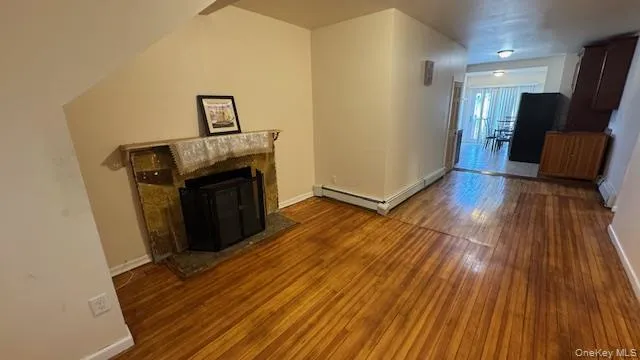 Unfurnished living room with a fireplace, dark wood-type flooring, and a baseboard heating unit Unfurnished living room with a fireplace, dark wood-type flooring, and a baseboard heating unit