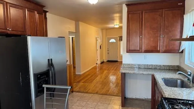 Kitchen with stainless steel refrigerator with ice dispenser, light stone counters, black gas stove, and brown cabinetry Kitchen with stainless steel refrigerator with ice dispenser, light stone counters, black gas stove, and brown cabinetry
