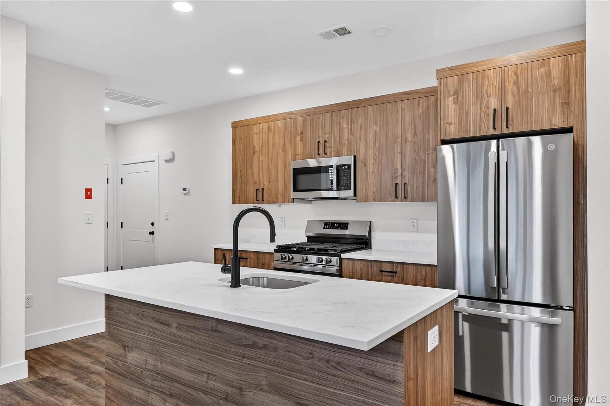 Kitchen with appliances with stainless steel finishes, a center island with sink, brown cabinets, light stone countertops, and recessed lighting Kitchen with appliances with stainless steel finishes, a center island with sink, brown cabinets, light stone countertops, and recessed lighting