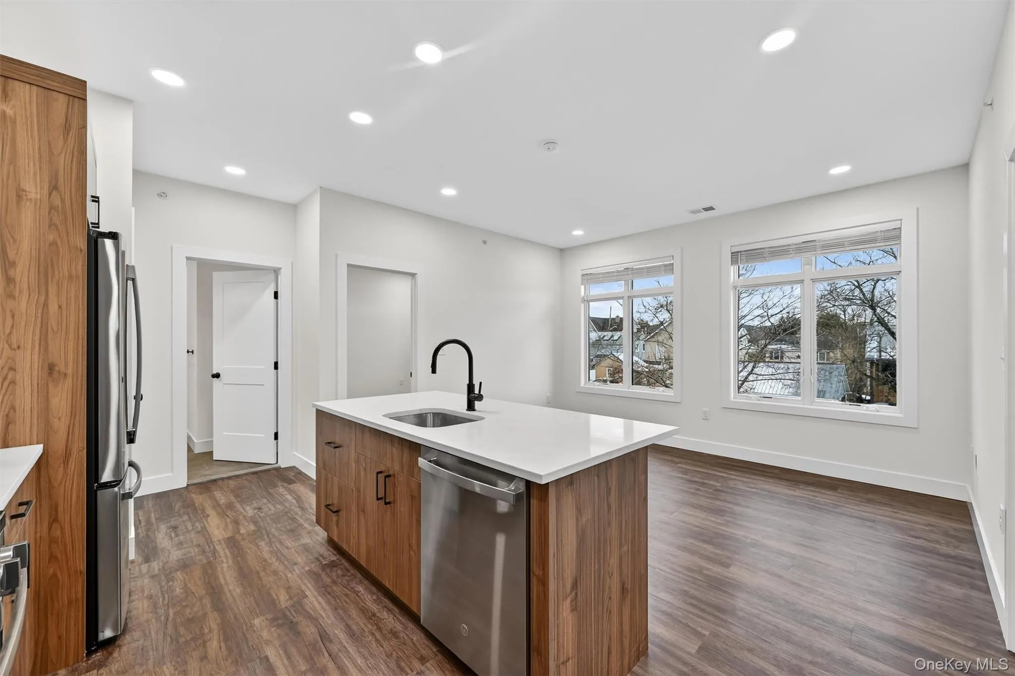 Kitchen featuring brown cabinets, stainless steel appliances, a center island with sink, light stone countertops, and dark wood-style floors Kitchen featuring brown cabinets, stainless steel appliances, a center island with sink, light stone countertops, and dark wood-style floors