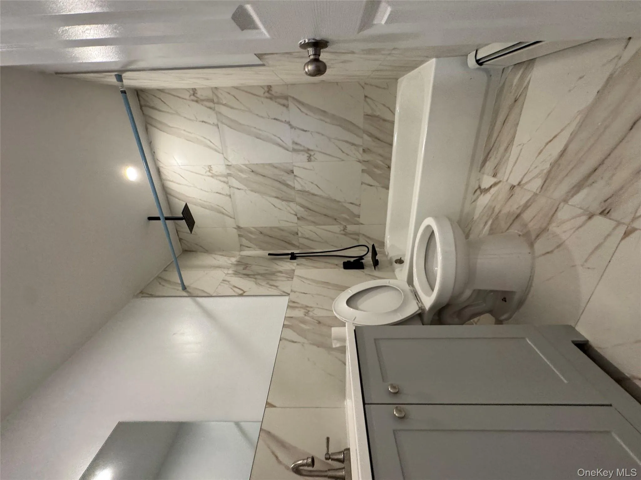 Bathroom with vanity, a combined bath / shower with rainfall shower, tile walls, light marble finish floors, and a baseboard radiator Bathroom with vanity, a combined bath / shower with rainfall shower, tile walls, light marble finish floors, and a baseboard radiator