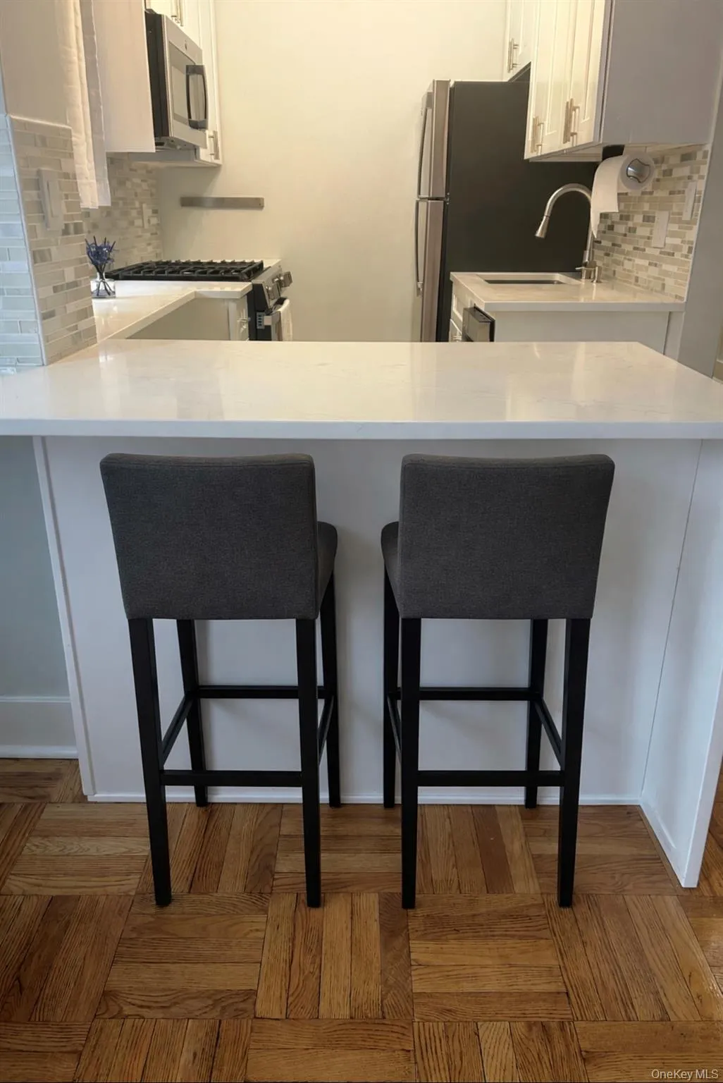Kitchen featuring decorative backsplash, white cabinetry, a peninsula, light stone counters, and a kitchen bar Kitchen featuring decorative backsplash, white cabinetry, a peninsula, light stone counters, and a kitchen bar