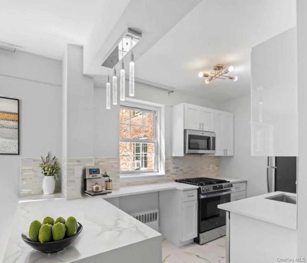 Kitchen with appliances with stainless steel finishes, white cabinets, light stone counters, light marble finish flooring, and a chandelier Kitchen with appliances with stainless steel finishes, white cabinets, light stone counters, light marble finish flooring, and a chandelier