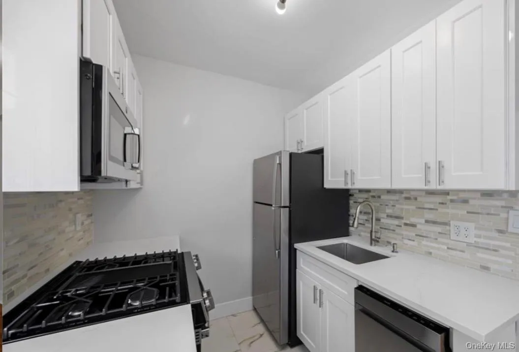 Kitchen featuring backsplash, appliances with stainless steel finishes, white cabinets, and light marble finish flooring Kitchen featuring backsplash, appliances with stainless steel finishes, white cabinets, and light marble finish flooring