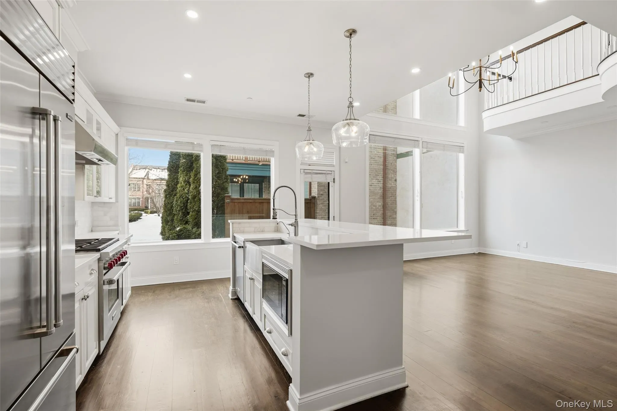 Kitchen featuring built in appliances, pendant lighting, white cabinetry, a kitchen island with sink, and light stone countertops Kitchen featuring built in appliances, pendant lighting, white cabinetry, a kitchen island with sink, and light stone countertops