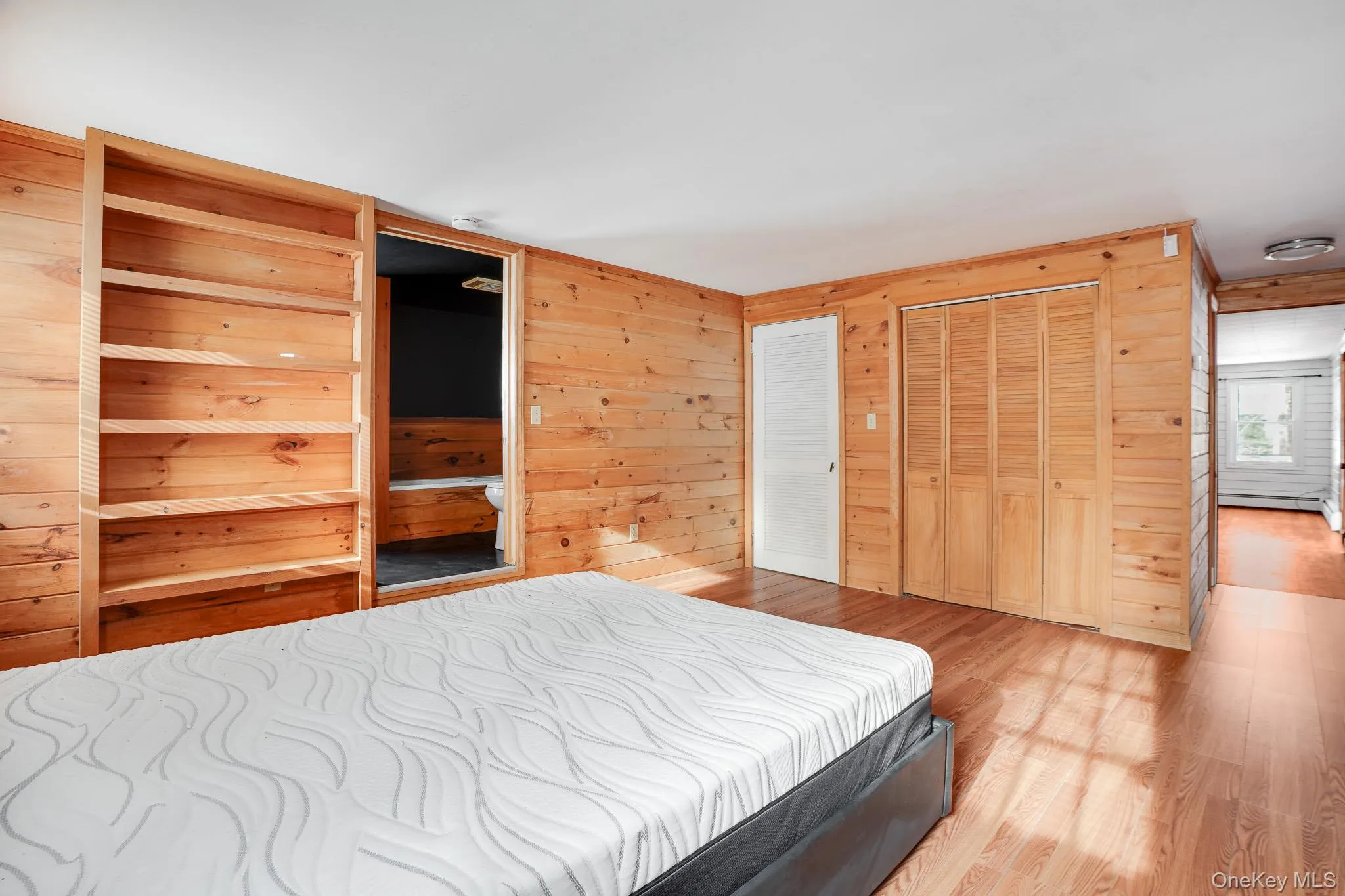 Bedroom with wooden walls, wood finished floors, a closet, and a baseboard radiator Bedroom with wooden walls, wood finished floors, a closet, and a baseboard radiator