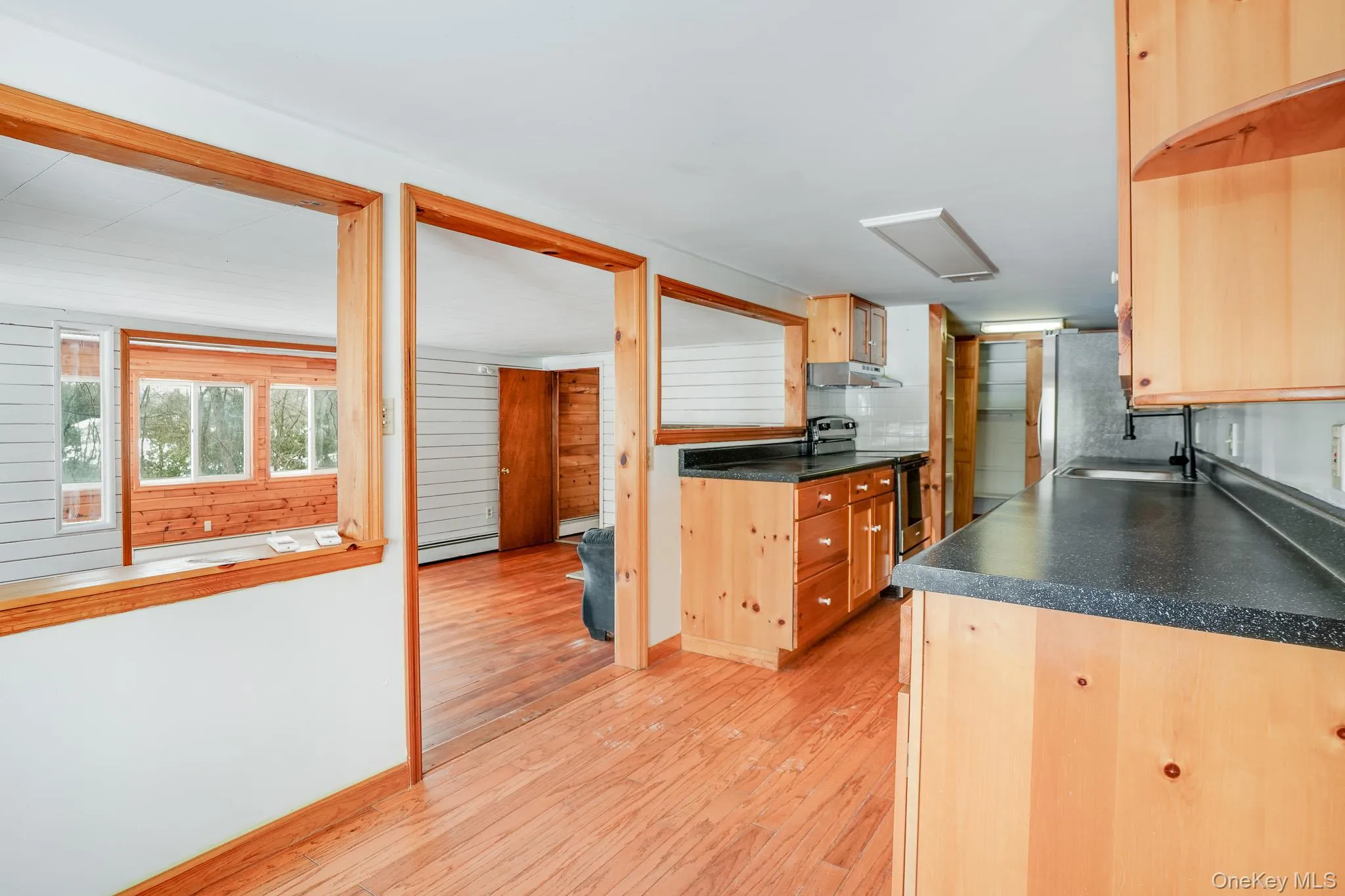 Kitchen with dark countertops, electric stove, light wood-style flooring, open shelves, and under cabinet range hood Kitchen with dark countertops, electric stove, light wood-style flooring, open shelves, and under cabinet range hood