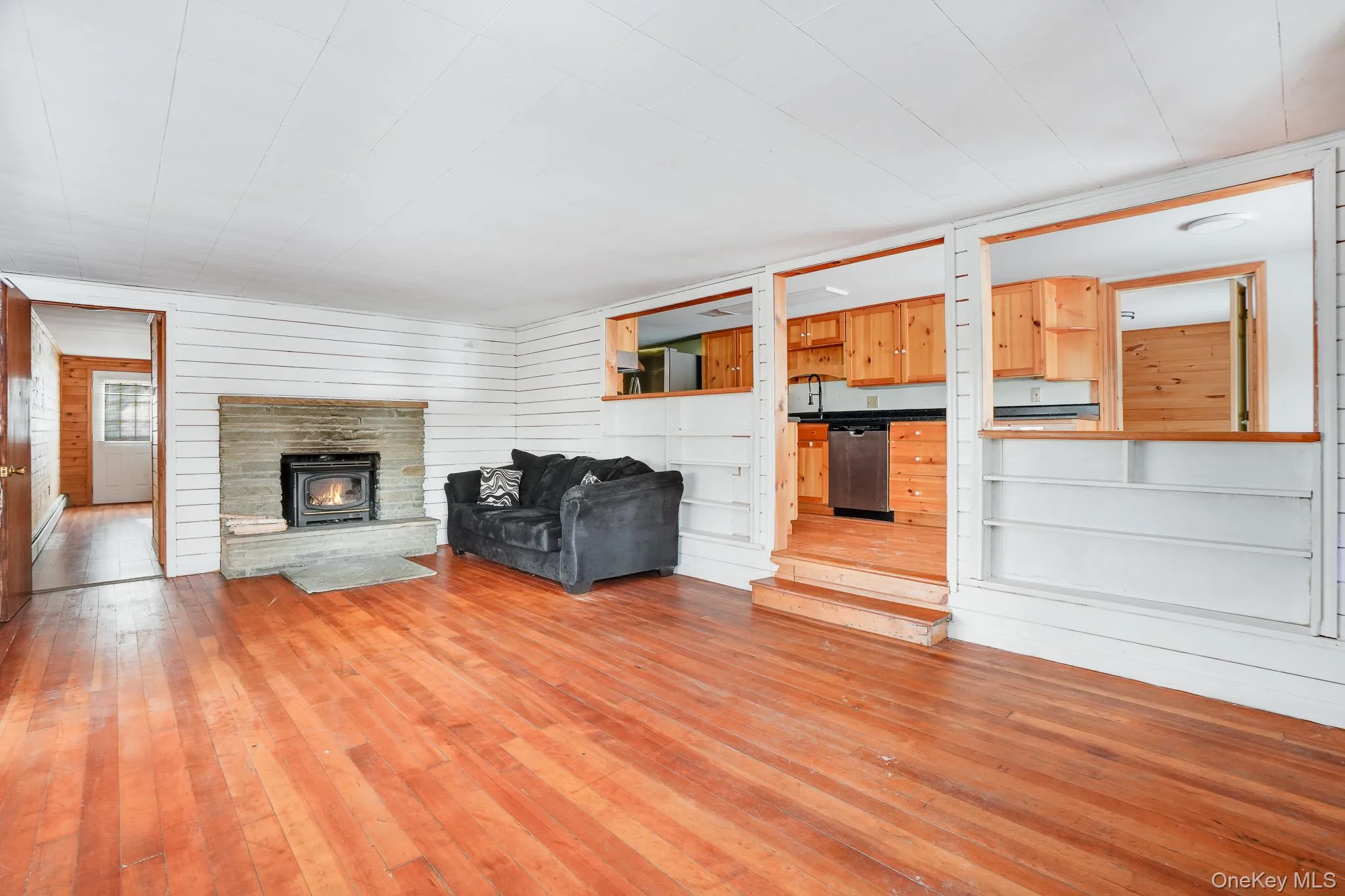 Unfurnished living room featuring wood walls, hardwood / wood-style floors, and a baseboard radiator Unfurnished living room featuring wood walls, hardwood / wood-style floors, and a baseboard radiator