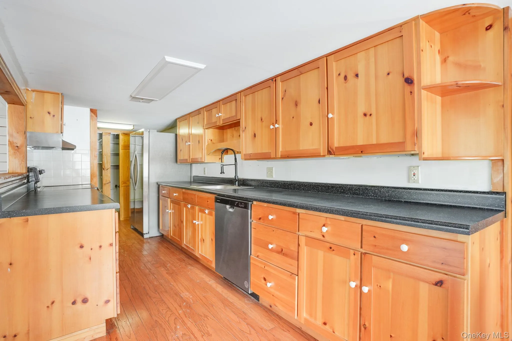 Kitchen featuring dark countertops, light wood-style floors, open shelves, and stainless steel appliances Kitchen featuring dark countertops, light wood-style floors, open shelves, and stainless steel appliances