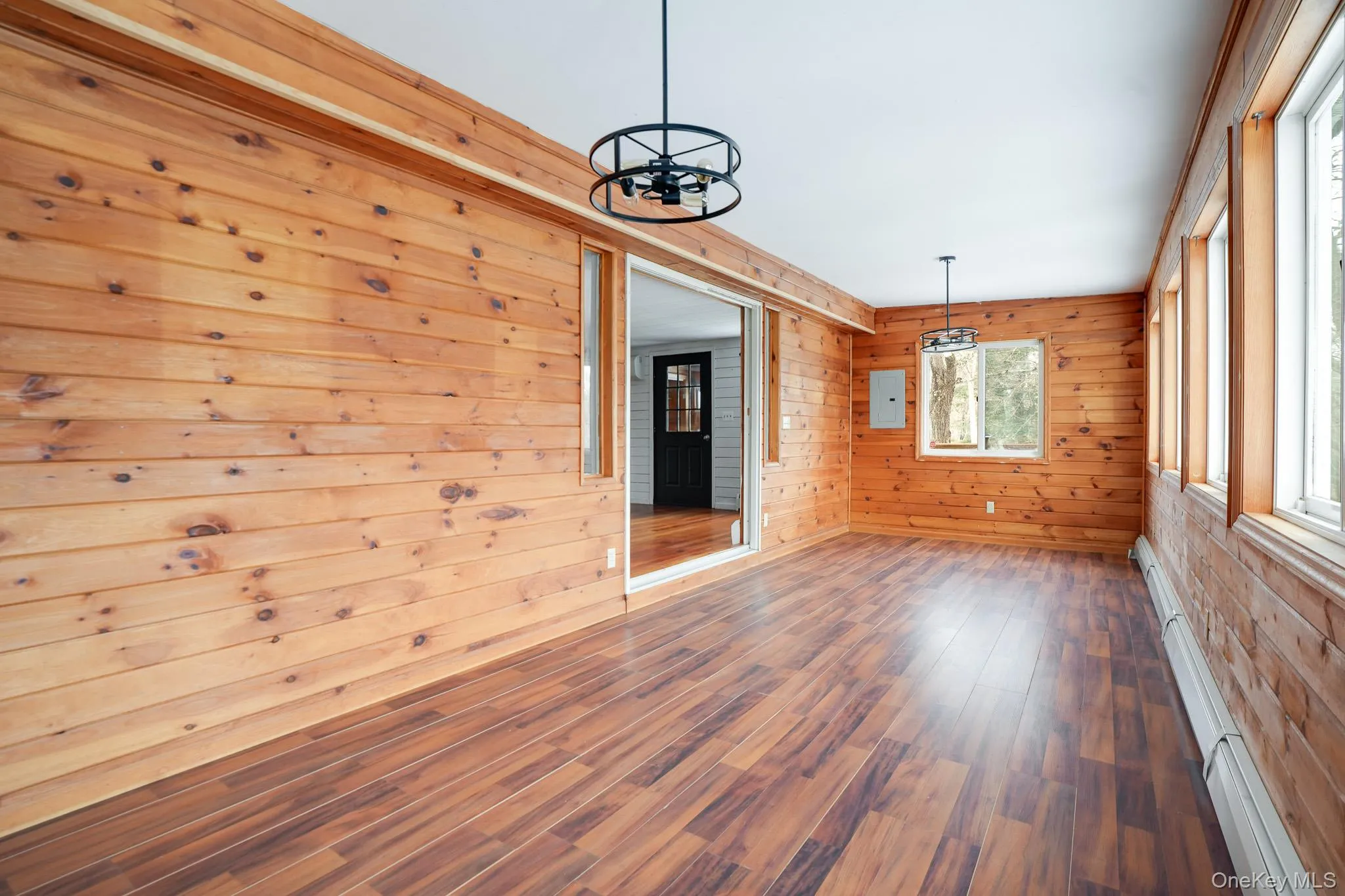 Unfurnished room with baseboard heating, wood walls, wood finished floors, a chandelier, and electric panel Unfurnished room with baseboard heating, wood walls, wood finished floors, a chandelier, and electric panel