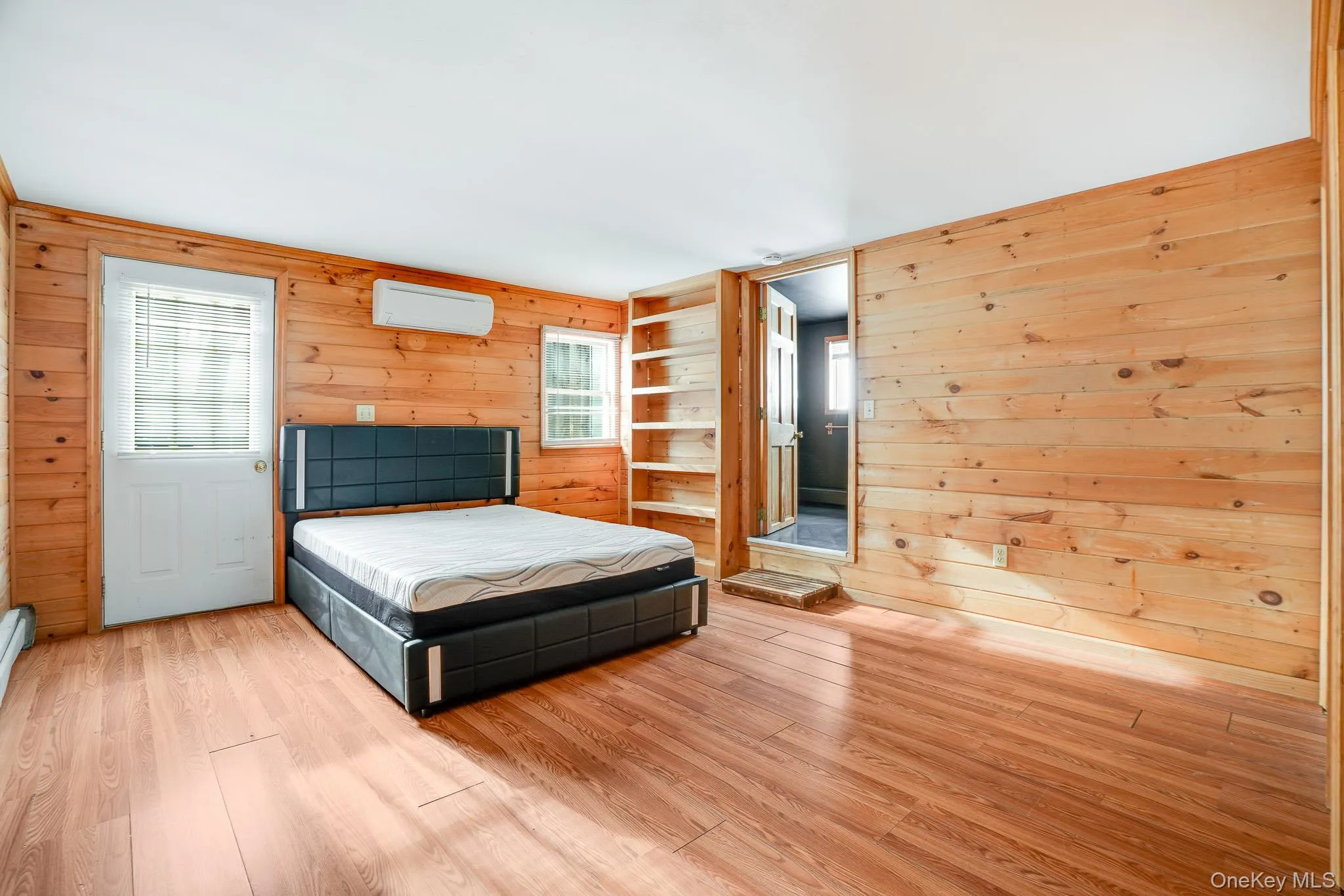 Bedroom with wooden walls, wood finished floors, and a wall mounted AC Bedroom with wooden walls, wood finished floors, and a wall mounted AC