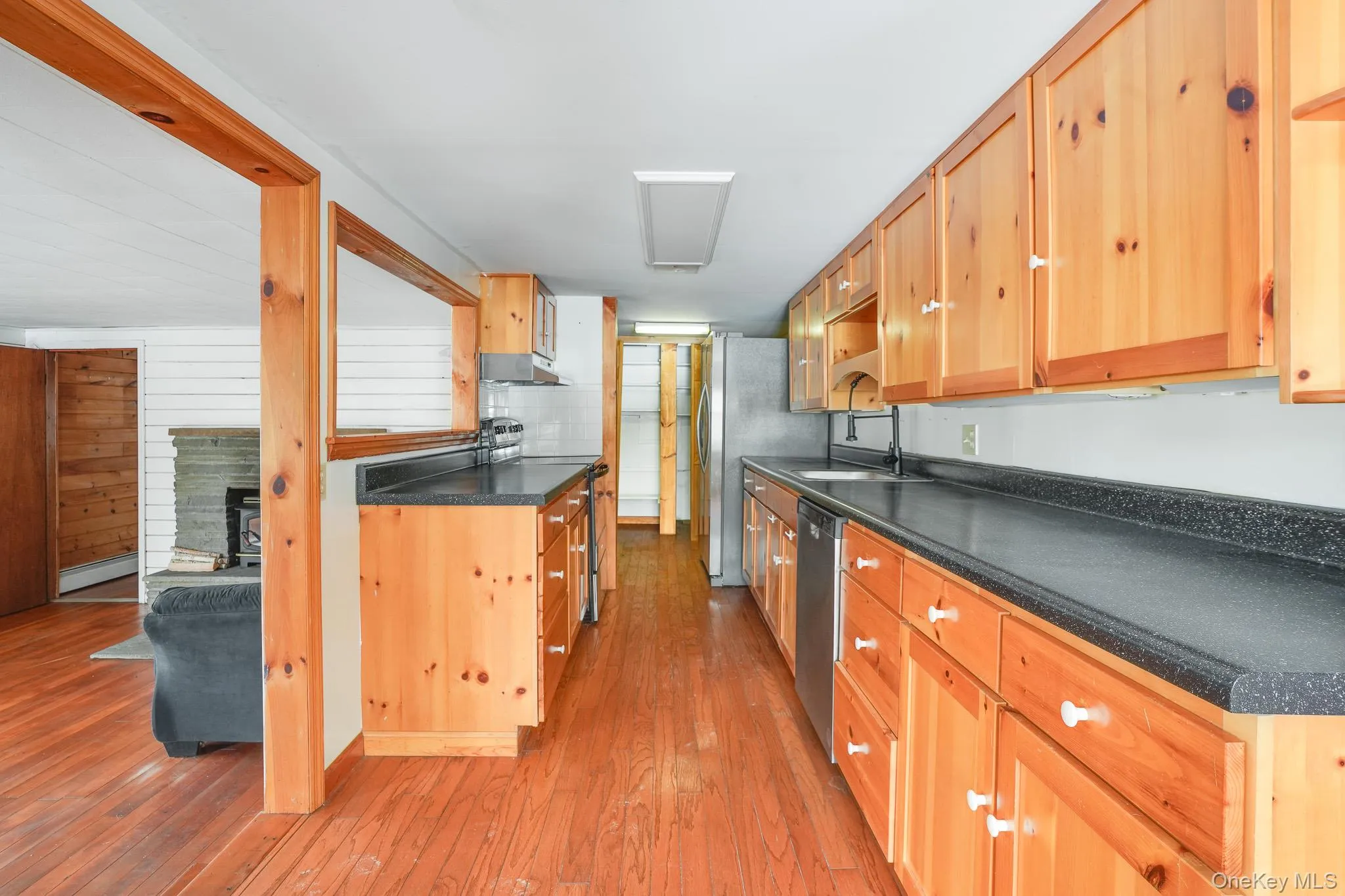 Kitchen featuring dark countertops, stainless steel appliances, light wood finished floors, under cabinet range hood, and light brown cabinets Kitchen featuring dark countertops, stainless steel appliances, light wood finished floors, under cabinet range hood, and light brown cabinets