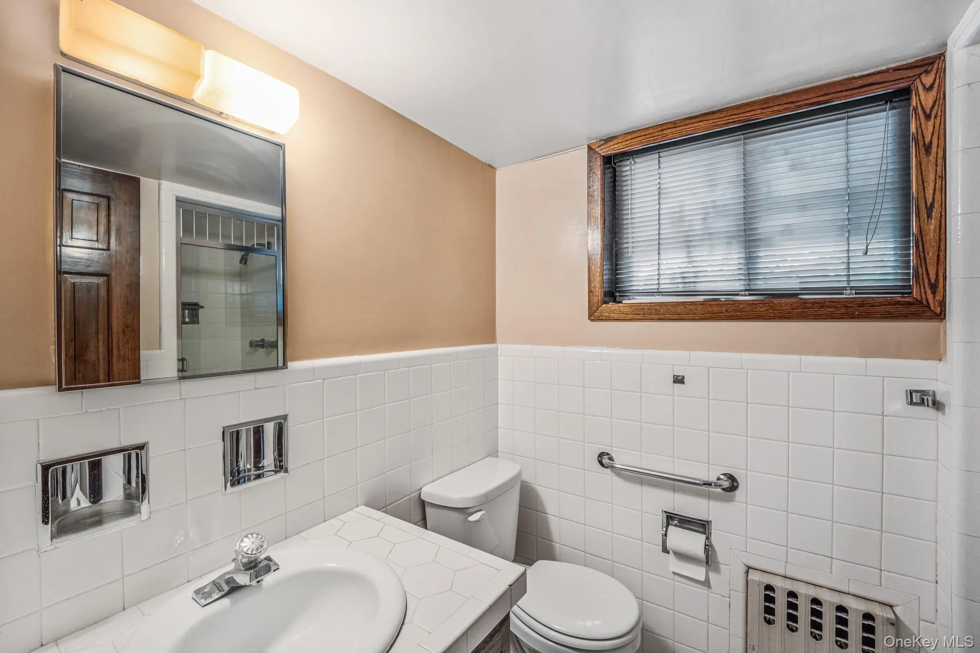 Full bathroom with a tile shower, vanity, radiator heating unit, tile walls, and a wainscoted wall Full bathroom with a tile shower, vanity, radiator heating unit, tile walls, and a wainscoted wall