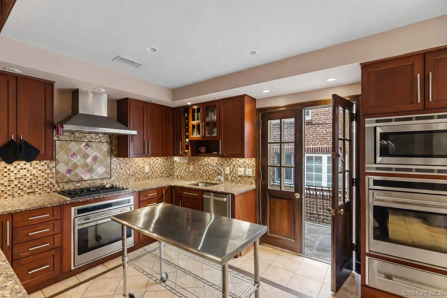 Kitchen featuring light stone countertops, appliances with stainless steel finishes, wall chimney exhaust hood, a warming drawer, and recessed lighting Kitchen featuring light stone countertops, appliances with stainless steel finishes, wall chimney exhaust hood, a warming drawer, and recessed lighting