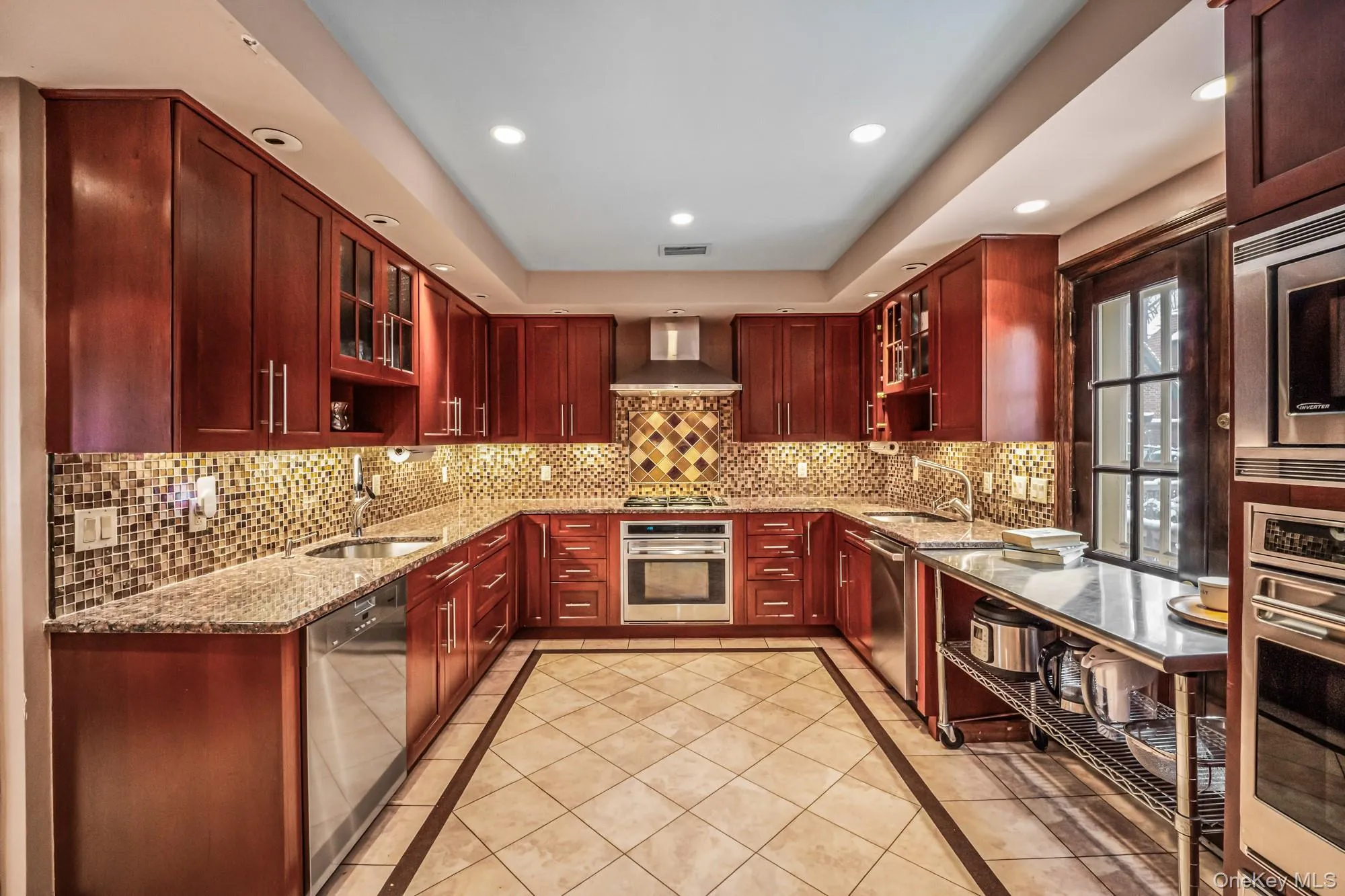 Kitchen with reddish brown cabinets, glass insert cabinets, inlaid floor details, light stone counters, and a raised ceiling Kitchen with reddish brown cabinets, glass insert cabinets, inlaid floor details, light stone counters, and a raised ceiling