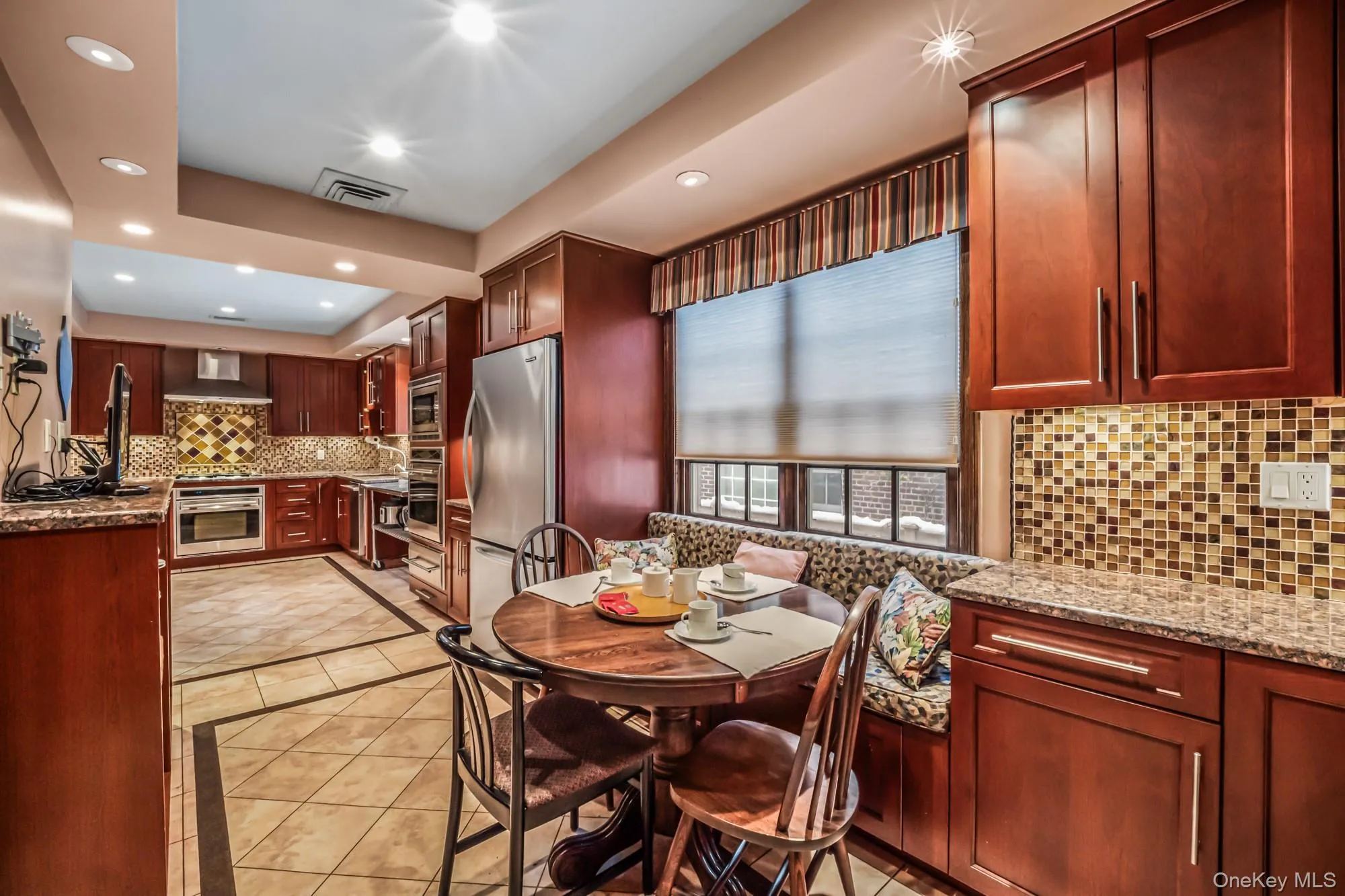 Kitchen with light stone counters, backsplash, reddish brown cabinets, stainless steel appliances, and recessed lighting Kitchen with light stone counters, backsplash, reddish brown cabinets, stainless steel appliances, and recessed lighting