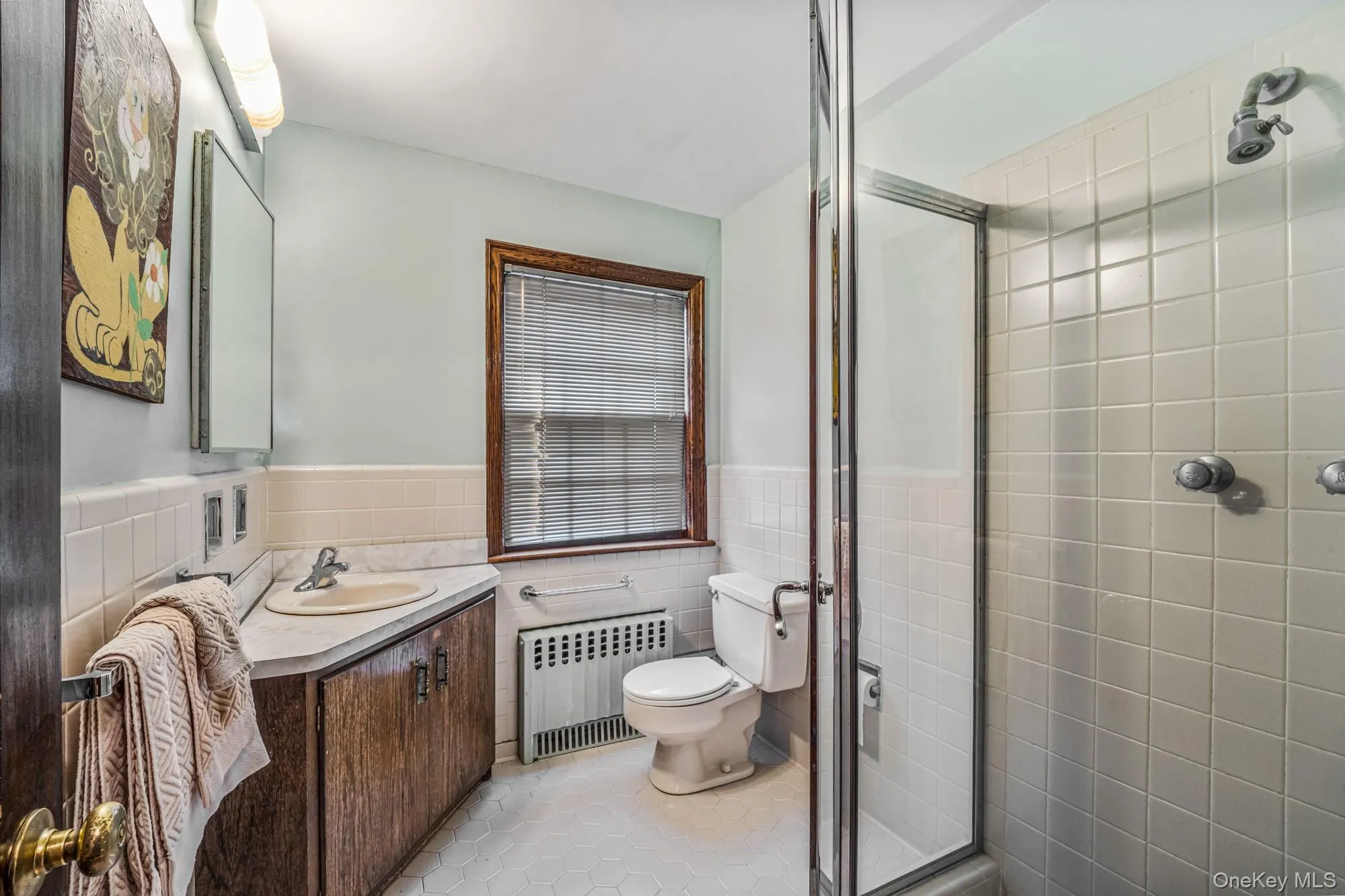 Bathroom with vanity, radiator, light tile patterned flooring, a stall shower, and a wainscoted wall Bathroom with vanity, radiator, light tile patterned flooring, a stall shower, and a wainscoted wall