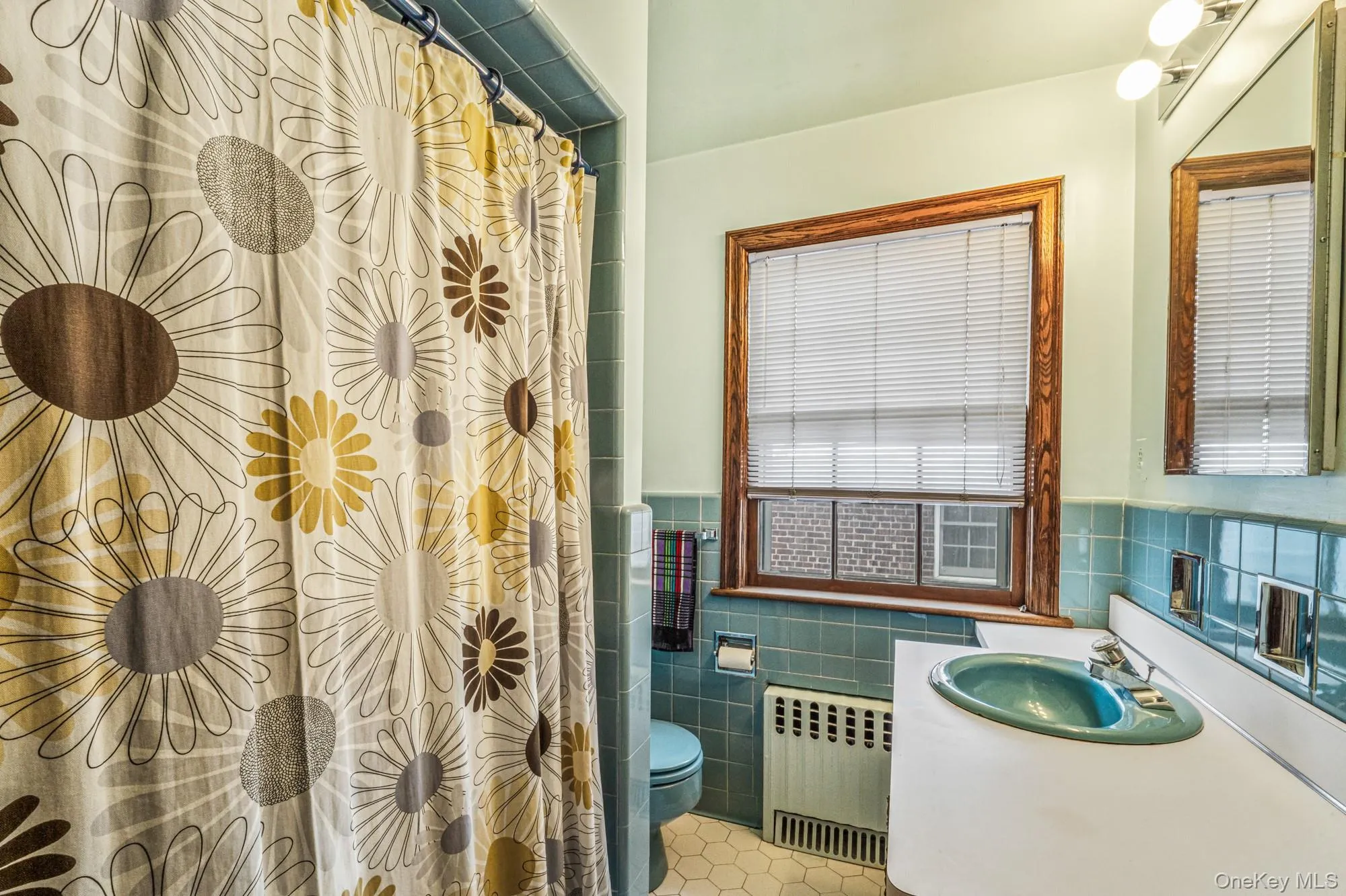 Bathroom with radiator, vanity, a shower with shower curtain, tile walls, and wainscoting Bathroom with radiator, vanity, a shower with shower curtain, tile walls, and wainscoting