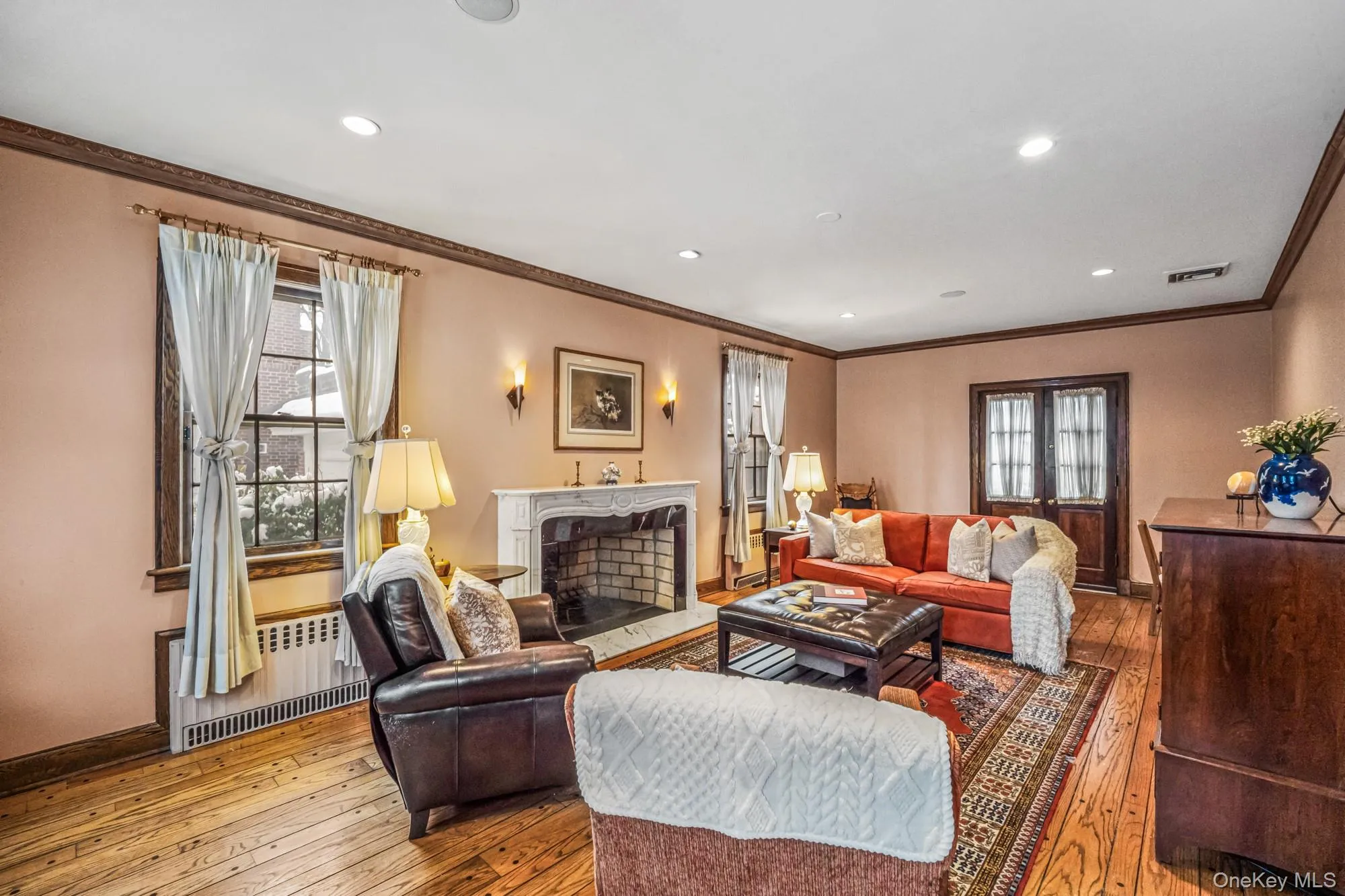 Living room with a premium fireplace, wood-type flooring, radiator heating unit, ornamental molding, and recessed lighting Living room with a premium fireplace, wood-type flooring, radiator heating unit, ornamental molding, and recessed lighting