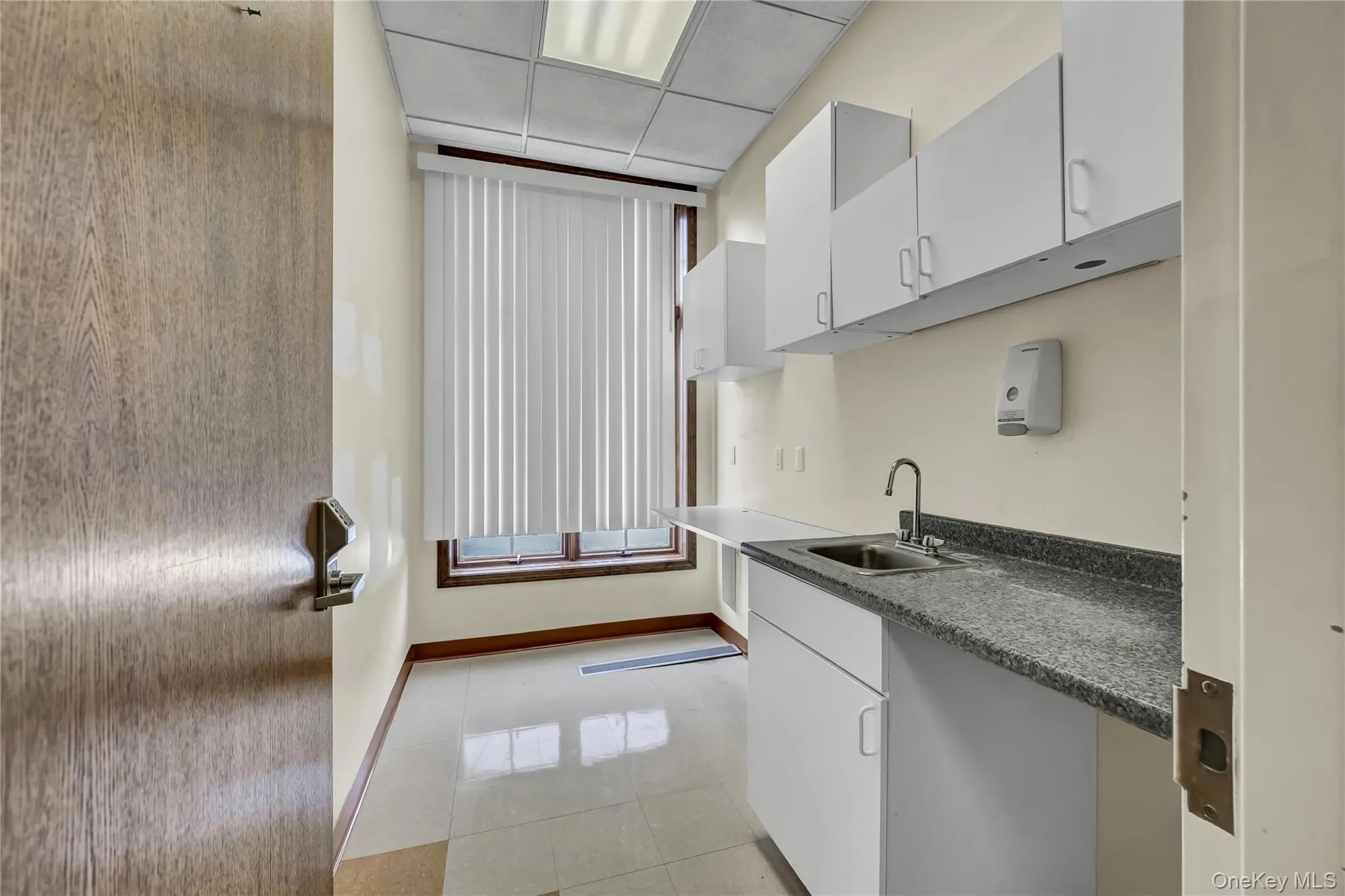 Kitchen featuring white cabinets, light tile patterned flooring, a paneled ceiling, and dark countertops Kitchen featuring white cabinets, light tile patterned flooring, a paneled ceiling, and dark countertops