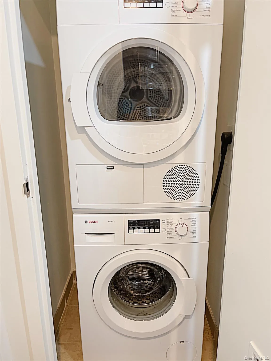 Laundry area with stacked washer / dryer and light tile patterned floors Laundry area with stacked washer / dryer and light tile patterned floors