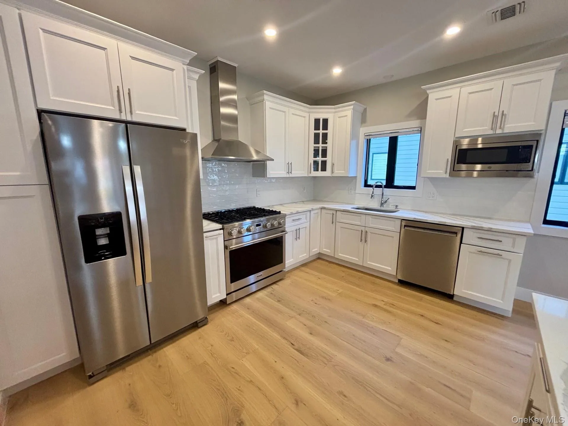 Kitchen with stainless steel appliances, wall chimney range hood, white cabinets, and recessed lighting Kitchen with stainless steel appliances, wall chimney range hood, white cabinets, and recessed lighting
