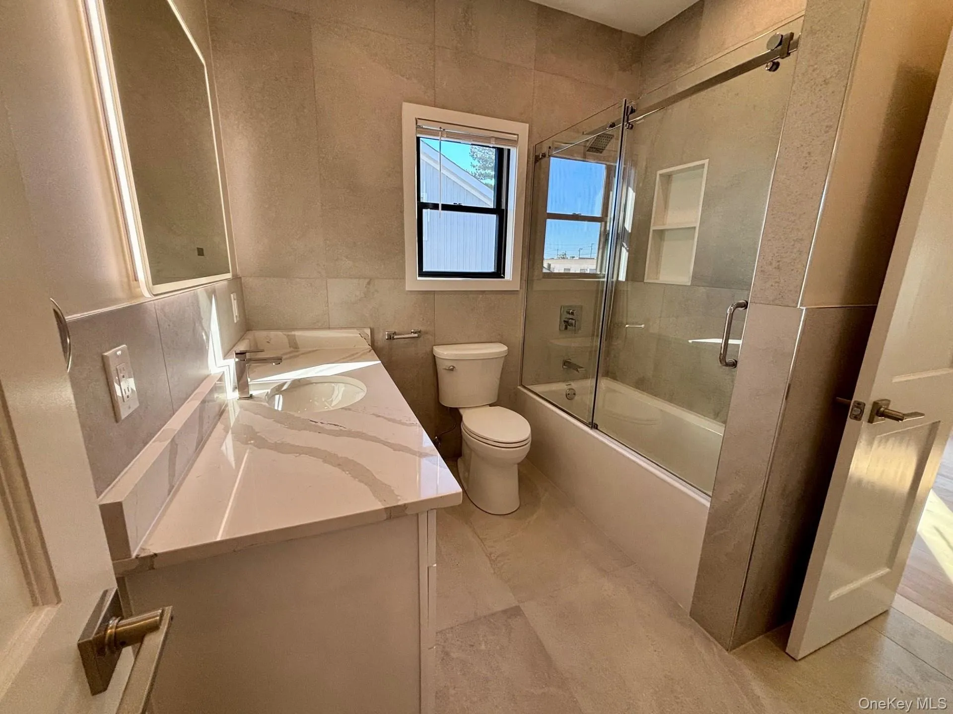 Full bath with tile walls, bath / shower combo with glass door, and vanity Full bath with tile walls, bath / shower combo with glass door, and vanity